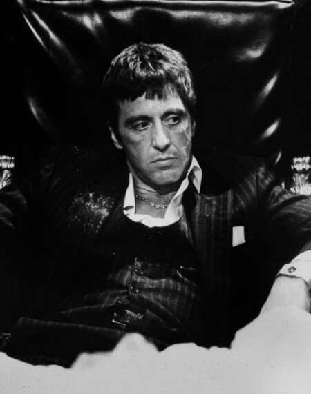Photo noir et blanc d'Al Pacino (Tony Montana) assis pensivement en smoking à un bureau luxueux dans Scarface, main sur le menton.