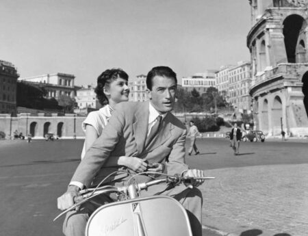 Photographie en noir et blanc d'Audrey Hepburn et Gregory Peck sur un scooter Vespa devant le Colisée à Rome, tirée du film Vacances Romaines.