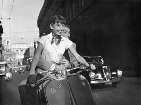 Affiche Audrey Hepburn - Rome : Gros plan en noir et blanc d'Audrey Hepburn riant aux éclats au guidon d'une Vespa, avec Gregory Peck derrière elle, dans une rue de Rome.