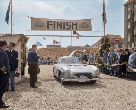 Photographie historique colorisée de 1957 montrant une Mercedes-Benz 300 SL argentée aux portes "papillon" ouvertes, franchissant la ligne d'arrivée d'une épreuve automobile devant une foule.