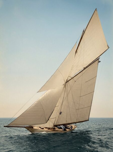 Photographie historique colorisée montrant un majestueux voilier de régate classique, toutes voiles dehors (portant le numéro 8), naviguant sur l'océan.
