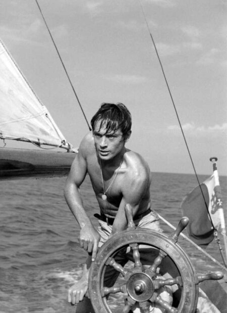 Affiche Delon Plein Soleil en noir et blanc : l'acteur Alain Delon torse nu manœuvre la barre d'un bateau en mer.