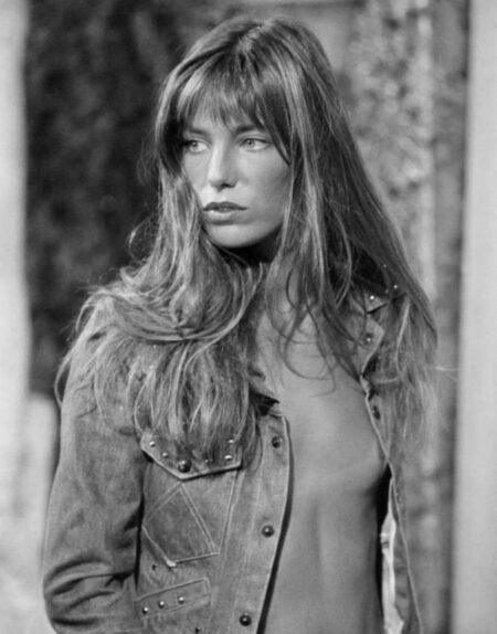Photographie en noir et blanc de Jane Birkin avec sa célèbre frange, nue sous sa chemise en jean entrouverte.