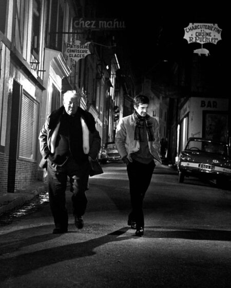Plan large de nuit montrant Jean Gabin et Jean-Paul Belmondo marchant ensemble dans une rue vide éclairée par des enseignes dans le film Un Singe en Hiver.
