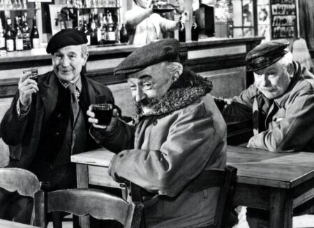Jean Gabin, Pierre Fresnais et Noël-Noël, portant des casquettes, riant et buvant du vin rouge attablés dans un bistro, scène du film Les Vieux de la Vieille.