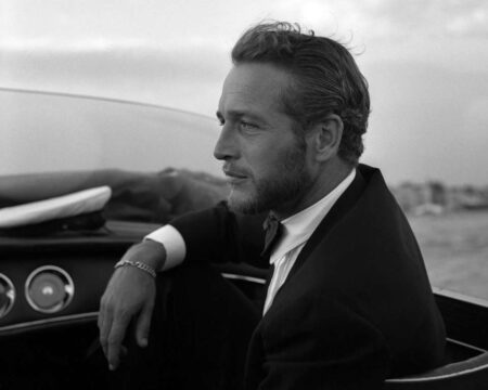 Photographie de profil en noir et blanc de Paul Newman en 1963 à Venise. L'acteur, portant une barbe courte et vêtu d'un costume élégant avec nœud papillon, regarde vers l'horizon depuis un bateau naviguant sur la lagune.