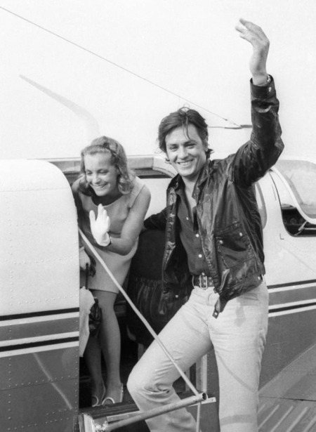 Affiche Delon Romy Schneider : photographie vintage en noir et blanc de 1968 montrant Alain Delon et Romy Schneider souriants, descendant d'un petit avion de tourisme.