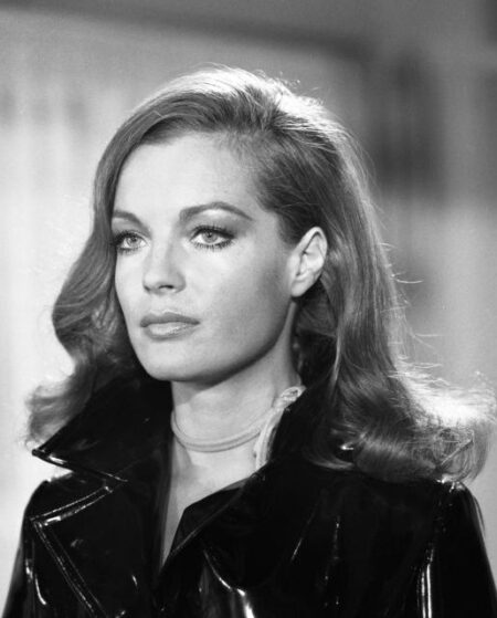 Photographie en noir et blanc de Romy Schneider dans le film Max et les Ferrailleurs, portant un manteau en vinyle brillant et un fin collier, regardant au loin avec une expression captivante.