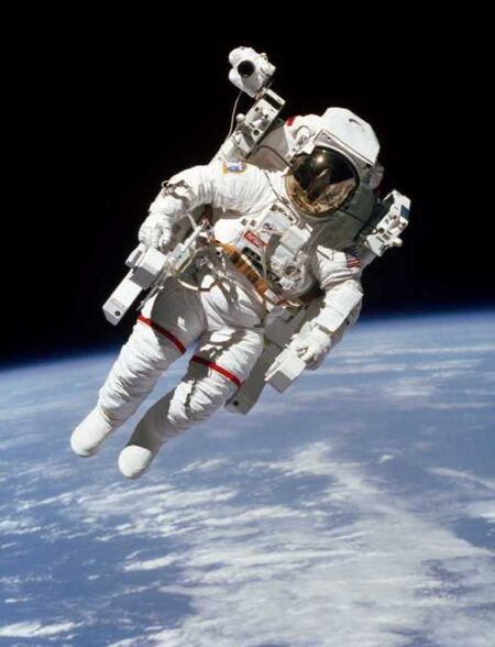 Photographie historique d'un astronaute flottant en apesanteur dans l'espace avec la courbure de la Terre et des nuages en arrière-plan.