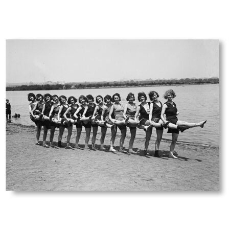 Affiche baigneuses années 20 : Photographie panoramique en noir et blanc des années 1920 montrant une longue file de femmes en maillots de bain d'époque sur une plage, levant toutes la jambe droite en même temps.