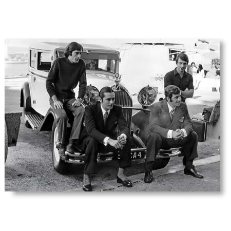Photographie de plateau en noir et blanc montrant Alain Delon et Jean-Paul Belmondo assis sur une voiture ancienne avec leurs frères respectifs pendant le tournage de Borsalino.