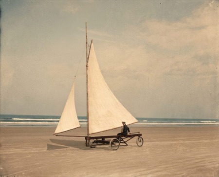 Affiche Char Voile Vintage : photographie du début du XXe siècle montrant un pionnier en uniforme sur un char à voile primitif sur une immense plage déserte.