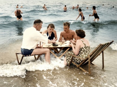 Affiche Pique-Nique Mer Vintage : photographie des années 30 montrant quatre personnes attablées dans l'eau de mer, prenant le thé ou le café au milieu des vagues sur une plage animée.