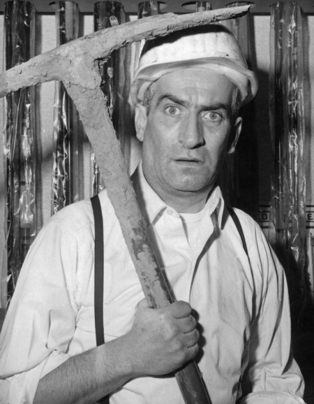 Affiche De Funès Banque : photographie d'art en noir et blanc de 1964 montrant Louis de Funès avec un casque de chantier et une pioche, tirée du film Faites sauter la banque.