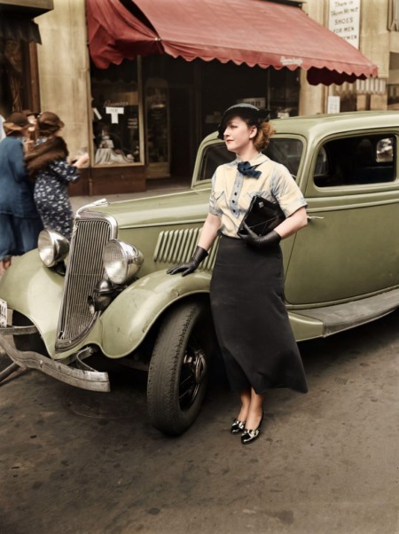 Affiche Mode Automobile Vintage Élégance : photographie d'art colorisée vers 1935 montrant une femme élégante en chapeau et gants posant à côté d'une Ford V8 verte des années 1930 dans une rue urbaine avec un auvent rouge.
