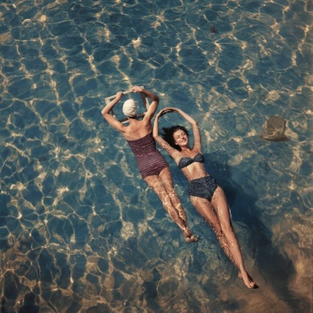 Affiche Mode Bain Vintage Piscine Miroir : photographie d’art colorisée vers 1940-1945 montrant deux femmes glamour flottant sur le dos dans une piscine claire, l'une tenant un miroir dans un cadre en bois et l'autre un maillot à pois type Pin-Up.