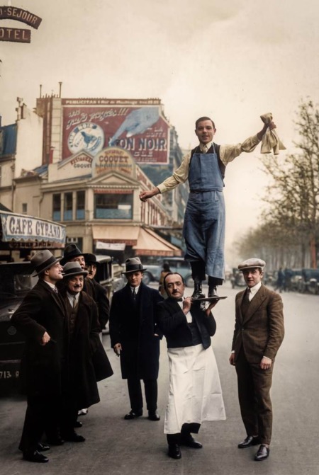 Affiche Garçon Café Paris Vintage : photographie d'art colorisée de 1929 montrant un serveur parisien portant son collègue sur un plateau de service suite à un pari perdu, devant le Café Gérard