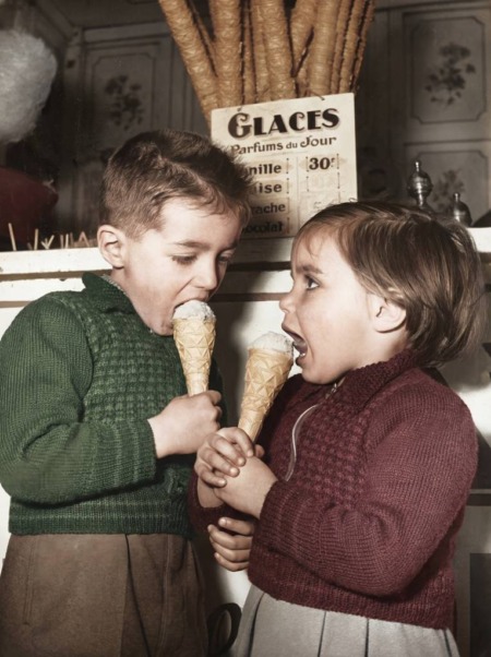 Affiche Enfants Glace Paris 1954 : photographie d'art colorisée montrant deux jeunes enfants en pulls de laine dégustant avec gourmandise un cornet de glace devant une échoppe parisienne en 1954.