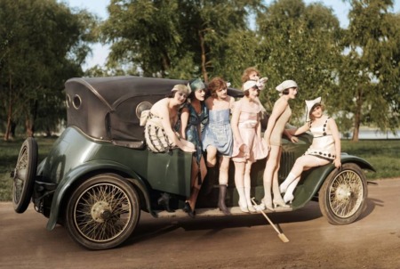 Photographie vintage colorisée des Années Folles représentant un groupe de jeunes femmes élégantes en maillots de bain d'époque posant devant une automobile ancienne, dans un parc ensoleillé.