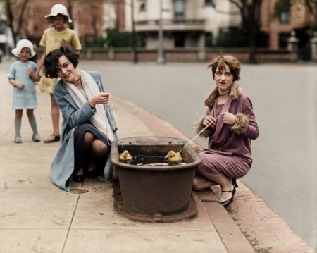 Photographie vintage colorisée de 1927 montrant deux jeunes femmes élégantes s'amusant à une pêche aux canards de rue devant des enfants.